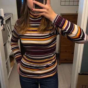 Randig polotröja från Amisu - Säljer en superfin randig polotröja från Amisu i storlek M. Tröjan har ett färgglatt mönster med ränder i svart, vit, lila, orange och gul. Den är långärmad och perfekt för höst och vinter. Materialet är mjukt och stretchigt, obs lite noppande
