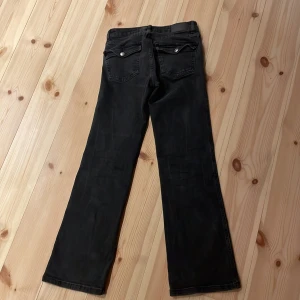 Svarta bootcut jeans från 157 - Säljer ett par svarta bootcut jeans från lager 157. De har en klassisk femficksdesign med snygga detaljer som silverfärgade knappar på bakfickorna. Perfekta för en avslappnad men stilren look!