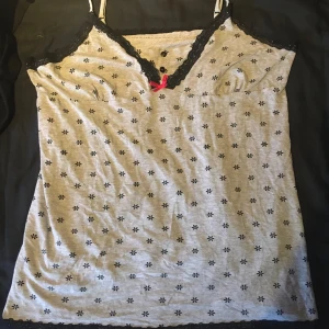 Linne - Snyggt grått linne med svarta blommor och en rosa rosett och svart spets köpt second hand och använts få gånger av mig. Vet inte märket. Fråga om du har frågor!