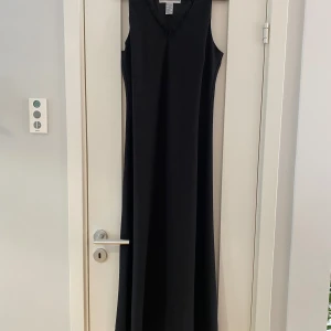 Svart lång armlös klänning med volang i kanterna i strl 14 från Jessica Howard - Svart lång armlös klänning med volang i kanterna i strl 14 från Jessica Howard.  Sparsamt använd och i fint begagnat skick.  Mått Över bröstet: ca 54 cm Längd från axeln och ner: ca 138 cm  100% polyester   Kommer från ett djur och rökfritt hem.