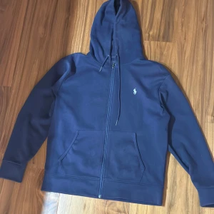 Ralph Lauren zip up hoodie marinblå - Tjena!  Nu säljer jag denna riktigt feta Ralph Lauren zip hoodie i färgen marinblå. Den är i dunder skick med knappt några tecken på användning utanför att ena av luv rep handtagen är intryckt. Storlek L. Priset kan diskuteras vid snabb affär:)  MVH 