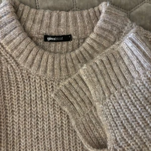 Beige stickad tröja från Gina Tricot - Säljer en supermysig beige stickad tröja med slits. Den har en loose passform med långa ärmar och ribbade detaljer vid hals, ärmslut och nederkant. Perfekt för höst och vinter när du vill hålla dig varm och stilren. 🧶✨