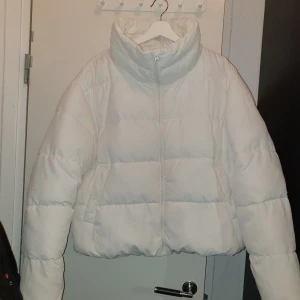 Vit pufferjacka  - Säljer en snygg och varm vit pufferjacka. Jackan har en hög krage och dragkedja framtill. Perfekt för kalla vinterdagar när du vill hålla dig varm och stilren. Den är i storlek XL men passar allt från M-XL beroende på hur man vill densitter. Som ny! 