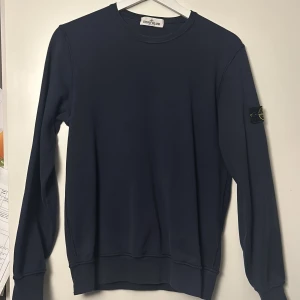 Mörkblå tröja från Stone Island Junior - Säljer en stilren mörkblå tröja från Stone Island Junior. Tröjan har en rund halsringning och långa ärmar. Den är dekorerad med det ikoniska Stone Island-märket på ärmen. Perfekt för en avslappnad och trendig look.Även äkta från Stone Island,kvitto finns ej för den e köpt för 5 års sen