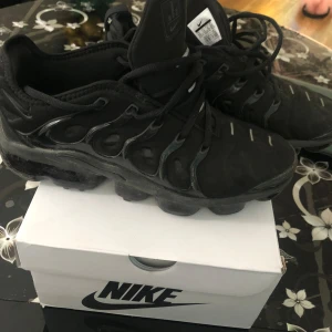 Svarta Nike sneakers - Säljer ett par svarta Nike sneakers med snörning och en robust sula. Skorna har en modern design med synliga luftkuddar i sulan för extra komfort. Perfekta för sommar, vår.