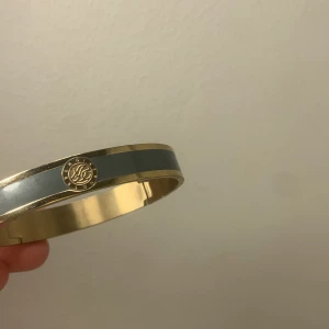 Guld- och svart armband - Elegant armband i guld med en svart rand och en dekorativ medaljongdetalj. Perfekt för att ge en stilren touch till din outfit.