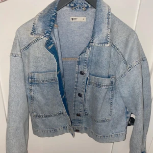 Ljusblå jeansjacka  - Snygg ljusblå jeansjacka från Gina i storlek S. Jackan har en klassisk design med knappar framtill och två stora fickor. Perfekt för en avslappnad stil.