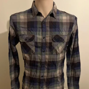 Rutig skjorta från edc - Snygg rutig skjorta från edc i olika nyanser av blått, grått och beige. Skjortan har långa ärmar och knappar framtill samt två bröstfickor med knappstängning. Perfekt för en avslappnad stil.