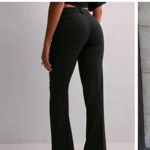 Snygga svarta kostymbyxor från Nelly med låg midja och flare passform. Byxorna har en klassisk design med knappar och dragkedja framtill. Perfekta för en stilren look. Orginal pris 400kr💕