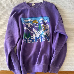 Lila sweatshirt från Urban outfitters - Säljer en lila sweatshirt från utban outfitters med ett färgglatt Aspen-tryck på framsidan. Tröjan har en rund halsringning och långa ärmar, perfekt för en avslappnad stil. Passar bra för kyligare dagar och ger en retro känsla. 🌟