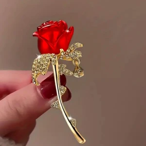 Brosch i form av en ros - Elegant brosch i form av en röd ros med guldfärgad stjälk och blad dekorerade med glittrande stenar. Perfekt för att ge en touch av glamour till din outfit.