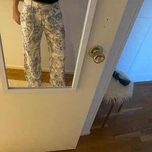 Blommiga byxor i vitt och blått - Snygga vita byxor med blått blommönster. De har en rak passform och är högmidjade, vilket ger en stilren look. Perfekta för att liva upp garderoben med lite mönster.