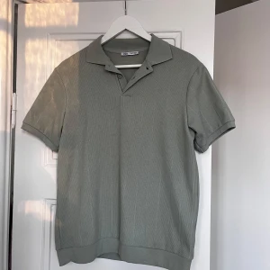 Grön pikétröja från Zara - Snygg grön pikétröja från Zara med klassisk krage och korta ärmar. Perfekt för en stilren och avslappnad look. Hör av dig vid minsta fråga eller fundering!
