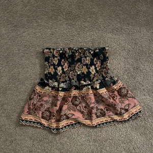 Blommig tubtopp-kjol - Charmig tubtopp-kjol med blommigt mönster i mörkblått och rosa. Kjolen har volanger och ett vackert paisley-mönster på den rosa delen. Perfekt för en bohemisk look.