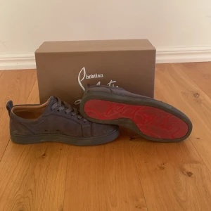Grå sneakers från Christian Louboutin - Snygga grå sneakers från Christian Louboutin med den ikoniska röda sulan. Skorna har en stilren design med snörning och är tillverkade i skinn. Perfekta för en trendig look. Allt på bild 5 följer med. 