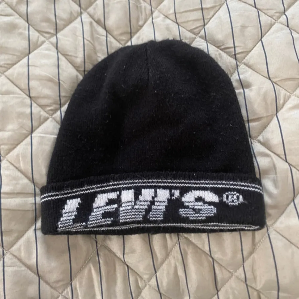 Snygg svart mössa från Levi's med vit logga och randdetalj. Perfekt för att hålla värmen med stil. Tillverkad i 100% akryl.. Asusteet.