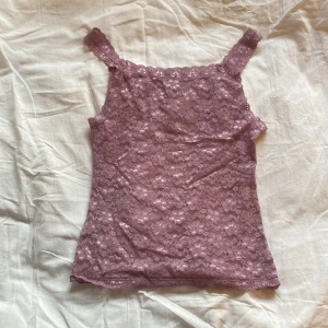 Rosa lila spetslinne - Säljer ett sött lila/rosa spetslinne med blommigt mönster. Linnet har breda axelband och är perfekt för varma dagar. Detaljerna i spetsen ger en romantisk känsla. Passar bra till både jeans och kjol.