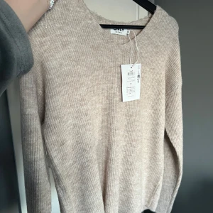 Stickad tröja med v-ringning  - Beige stickad tröja med v-ringning. Den första bilden visar tröjans riktiga färg. Helt ny med lapp kvar. Storlek XS. Nypris: 379kr🤍