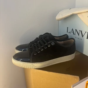 Svarta sneakers från Lanvin uk 10 - Snygga svarta sneakers från Lanvin med en kombination av mocka och lackdetaljer. Skorna har en vit sula och klassisk snörning. Perfekta för en stilren look. Uk 10 passar 44/45nyskick på dessa. og dustbag medföljer vid köp. Kan köpas utan og dustbag för billigare pris 