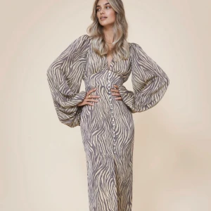 Zebramönstrad långklänning med vida ärmar - Snygg långklänning med zebramönster och vida ärmar från adoore. Klänningen har en djup v-ringning och knappar framtill. Perfekt till våren och sommaren. Använd cirka 3 gånger så nyskick!💗(liten i strlk så skulle snarare säga S)