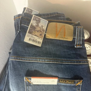 Blå jeans från Nudie Jeans w29L28 - Snygga blå jeans från Nudie Jeans i en klassisk femficksmodell. Tillverkade av 100% ekologisk bomull med en lätt tvättad look och orange sömmar. Perfekta för en avslappnad stil.
