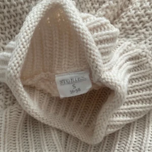 Beige stickad tröja från Stokke - Mysig beige stickad tröja från Stokke i storlek S. Tröjan har en hög krage och långa ärmar med ribbade muddar. Perfekt för kyliga dagar.