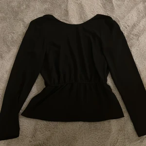 Svart långärmad blus med öppen rygg från NLY Trend - Snygg svart blus från NLY Trend med långa ärmar och en v-ringad design på ryggen. Perfekt för en stilren look. Toppen har en smickrande passform som definierar midjan 🤍