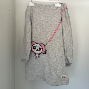 Grå hoodie från Toca Life x H&M - Säljer en grå hoodie från Toca Life x H&M med ett sött tryck av en tecknad figur framtill. Hoodien har en mönstrad insida i luvan med olika färgglada karaktärer. Perfekt för en avslappnad stil!