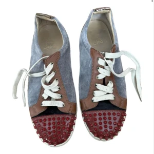 Ljusblåa Louboutin - Unika sneakers i grå mocka och brunt skinn med röda nitar på tån. Skorna har vita snören och en stilren design som sticker ut. 100% äkta! Riktigt feta Louboutins med unika färgkombinationer! Kom privat vid minsta fundering!