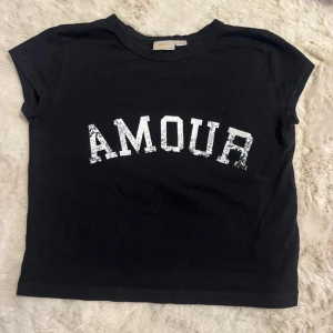 Svart t-shirt med tryck från Gina Tricot young - Snygg svart t-shirt från Gina Tricot med texten 'AMOUR' i vitt på framsidan. Den är använd få gånger och säljer för att den inte kommer till användning + har numera blivit för liten för mig. Storlek 134/140