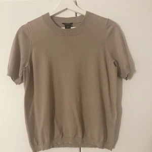 Beige kortärmad tröja från Lindex - Säljer en stilren beige/brun kortärmad tröja från Lindex. Tröjan har en rund halsringning och ribbade kanter vid ärmslut och nederkant. Perfekt för en avslappnad och elegant look.