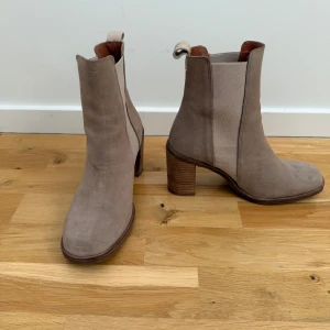 Beige chelsea boots med klack - Snygga beige chelsea boots i mocka med klack och elastiska paneler på sidorna för enkel på- och avtagning. Perfekta för en stilren look. Endast använda 1 gång, så i jättefint skick.
