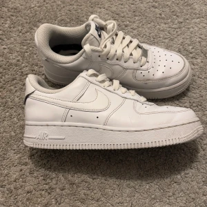 Nike Air Force 1 sneakers strl 35,5 - Klassiska vita Nike Air Force 1 sneakers med snörning . Skorna har en robust sula och ikonisk Nike-logga på sidan och hälen. Perfekta för en stilren look. Strl 35,5