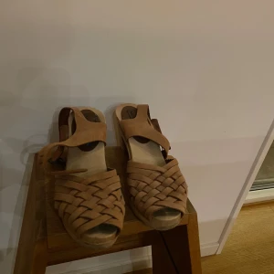 Klassiska Moheda Tofflor - Klassiska Moheda Tofflor, brun träskor med flätat mönster. Använda vid ett tillfälle. Klackhöjd: 7cm Storlek: 37