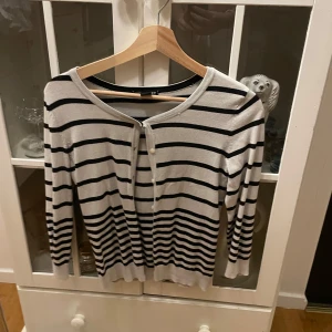 Randig kofta från H&M - Säljer en stilren randig kofta från H&M i svart och vit. Koftan har långa ärmar och knappar framtill. Perfekt för en avslappnad look.