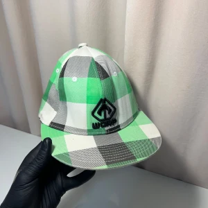 Grön och vit rutig keps från WCRP - Snygg keps med grönt och vitt rutmönster från WCRP. Kepsen har en broderad logga framtill och en klassisk passform. Perfekt för en avslappnad stil.