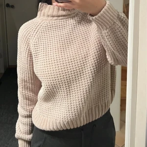 Beige stickad tröja - Mysig beige/puder rosa stickad tröja med hög krage och ett snyggt, texturerat mönster. i storlek S. Använd ett fåtal gånger, i väldigt bra skick. Modellen är storlek S. Väldigt varm och mysig tröja 