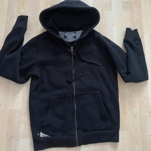 Svart hoodie med dragkedja - Säljer en klassisk svart hoodie med dragkedja och huva. Tröjan har långa ärmar och praktiska fickor framtill. Perfekt för en avslappnad stil.