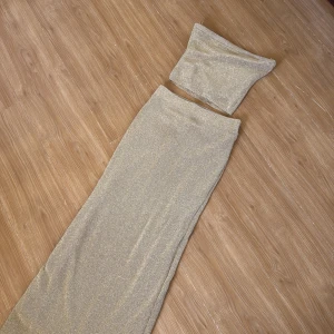 Glittrig guld tvådelad klänning  - Snygg tvådelad klänning i glittrigt guld från Gina tricot. Setet består av en axelbandslös topp och en långkjol, perfekt för en glamorös kväll. Materialet är stretchigt och bekvämt, vilket ger en smickrande passform. ✨priset gäller för både toppen och kjolen
