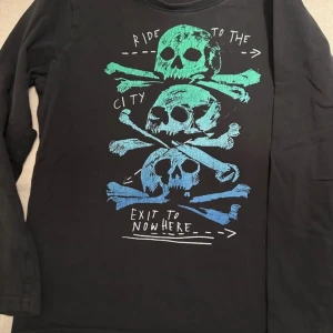 Svart långärmad tröja med dödskalletryck - Cool svart långärmad tröja med ett färgglatt dödskalletryck i grönt och blått. Texten 'Ride to the city, exit to nowhere' ger en edgy känsla. Perfekt för en avslappnad stil.