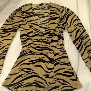 Zebramönstrad topp från Gina Tricot - Snygg zebramönstrad topp från Gina Tricot i beige och svart. Toppen har en omlott-design med långa ärmar och en v-ringad hals. Perfekt för att sticka ut med stil! 🖤