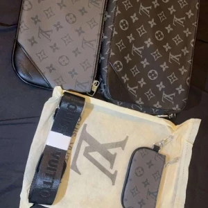 Lv trio axelväska  - Säljer en HELT NY snygg axelväska från Louis Vuitton med klassiskt monogrammönster i grått och svart. Väskan har en justerbar axelrem och dragkedja. Perfekt för att bära dina essentials med stil. PRISET KAN DISKUTERAS!!