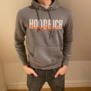 Grå hoodie från Hoodrich - Säljer en snygg grå hoodie från Hoodrich med tryck i vitt och orange på bröstet. Tröjan har en klassisk känguruficka och justerbar huva med snören. Perfekt för en avslappnad stil. Modellen är 183 och det står på tröjan att den är XS men lutar mer åt S/M pris är diskuterbart👍