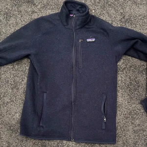 Mörkblå fleecejacka från Patagonia - Säljer en mörkblå fleecejacka från Patagonia med dragkedja framtill i storlek M. Jackan har praktiska fickor med dragkedja och en broderad logotyp på bröstet. Perfekt för kyliga dagar! Nypris runt 1600. Inga defekter. Skick: 9/10. Tveka inte att höra av dig vid eventuella frågor. 