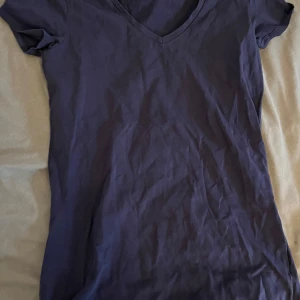 Mörkblå v-ringad t-shirt - Säljer en stilren mörkblå t-shirt med v-ringning. Perfekt för en avslappnad look. T-shirten har korta ärmar och är tillverkad i ett mjukt material.