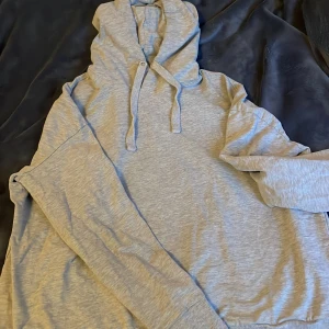 Grå hoodie  - Säljer en stilren grå hoodie. Den har en klassisk design med dragsko i huvan och långa ärmar. Perfekt för en avslappnad look.