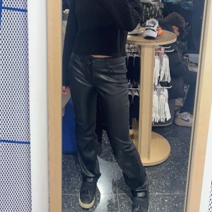 Svarta skinnbyxor - Snygga svarta skinnbyxor med en straight passform. Perfekta för en stilren look. Byxorna har en midwaist design och är tillverkade i ett glansigt skinnmaterial.