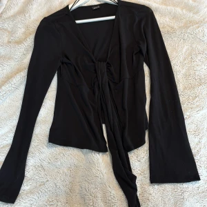 Svart långärmad knytblus - Snygg svart blus med långa ärmar och knytning framtill. Perfekt för en stilren look. Tillverkad i ett mjukt och bekvämt material från Gina tricot