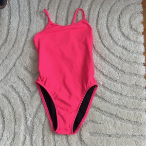 Rosa baddräkt från Jolyn - Snygg rosa baddräkt från Jolyn med smala axelband och öppen rygg. Perfekt för simträning eller en dag på stranden. Tillverkad i polyester för en bekväm passform och hållbarhet. Storlek 26( lite mindre än kaktus baddräkten). Nypris 800kr säljs för 180 kr.