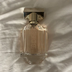 Parfym från Hugo Boss - Säljer min Hugo boss parfym, endast provad 1-2 gånger. I beskrivning på hemsidan står det Hugo Boss The Scent for Her är en lyxig och förförisk doft med en dragningskraft som inte går att motstå. Doften inleds med uppfriskande noter av persika och honung som genast väcker intresse. I hjärtat finns osmanthus absolute, en egensinnig blomsterdoft som också har en mörk och oväntad sida – precis som kvinnan som bär den. Kakao och vanilj bildar sedan en hypnotiskt elegant bas.  